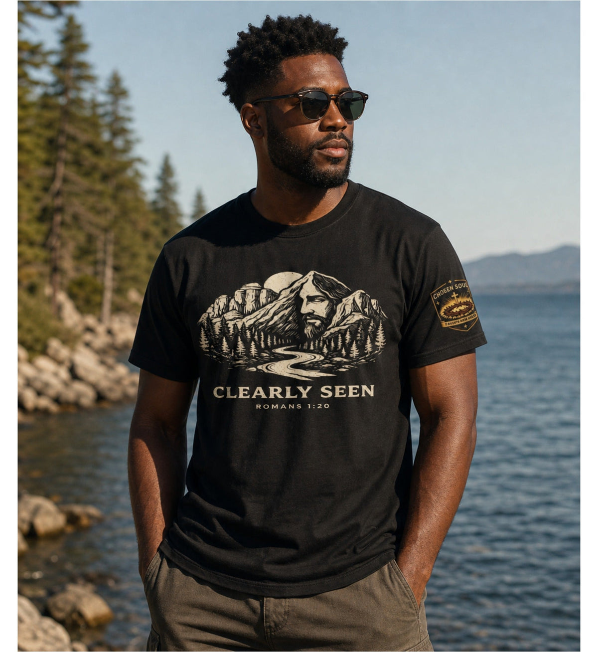 Man wearing Clearly Seen Romans 1:20 Comfort Colors 1717 Black Christian t-shirt by a mountain lake